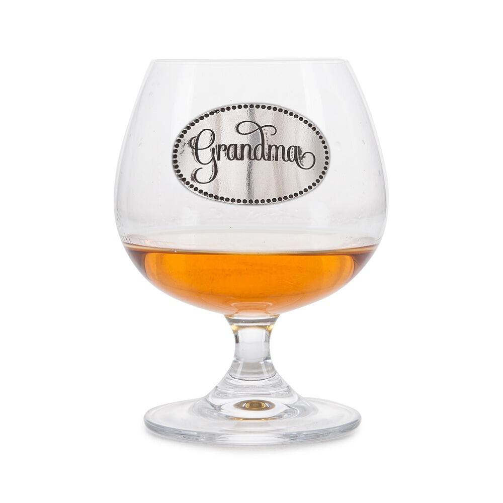 Crystal brandy glass with A E Williams pewter "Grandma" emblem, partially filled with amber liquid