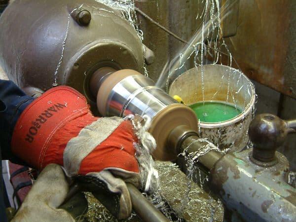 Metalworking lathe in action with a worker's gloved hand and coolant splashing