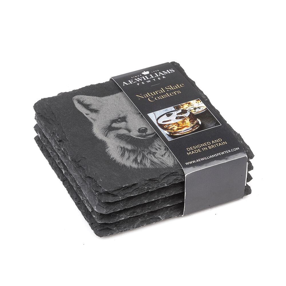 The top coaster features an engraved Fox design. A product label wraps around the stack, displaying the brand name, product type 'Natural Slate Coasters', and an image of a whiskey glass on a coaster. The label states 'Designed and Made in Britain' and includes the company website.