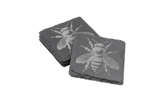 Two stacks of square slate coasters, each engraved with a detailed honeybee design.