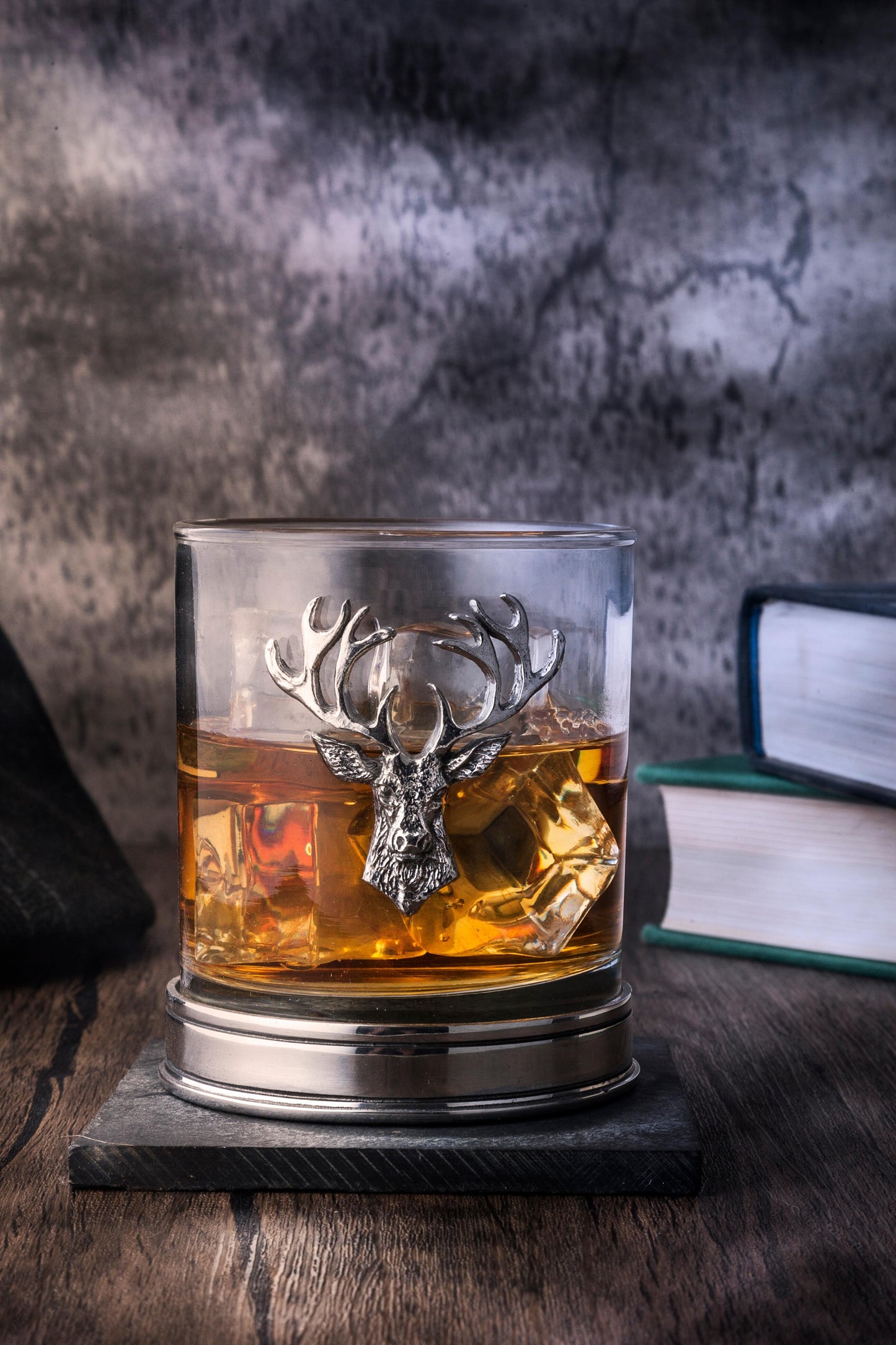 a whisky tumbler with a pewter stag icon and base filled with whisky on a wooden table