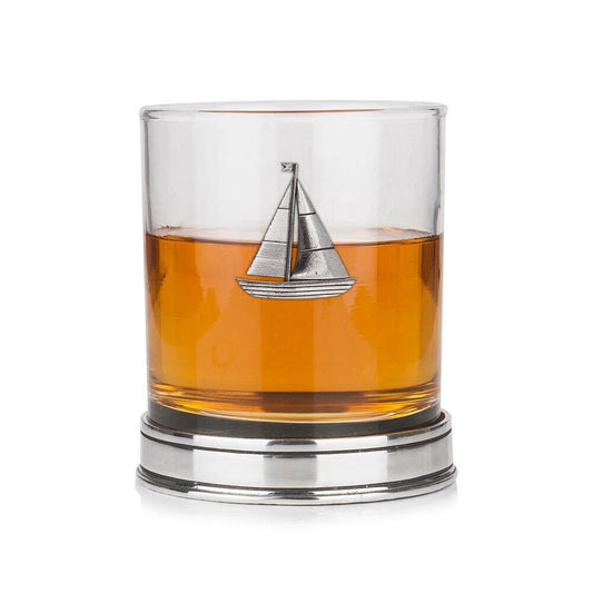 Whisky tumbler with pewter sailing boat emblem and polished base, partially filled with amber liquid