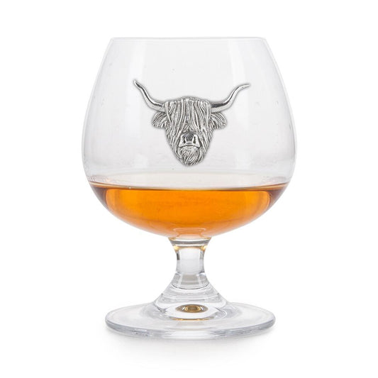 Crystal brandy snifter with pewter Highland Coo (Scottish cow) badge, partially filled with amber liquid