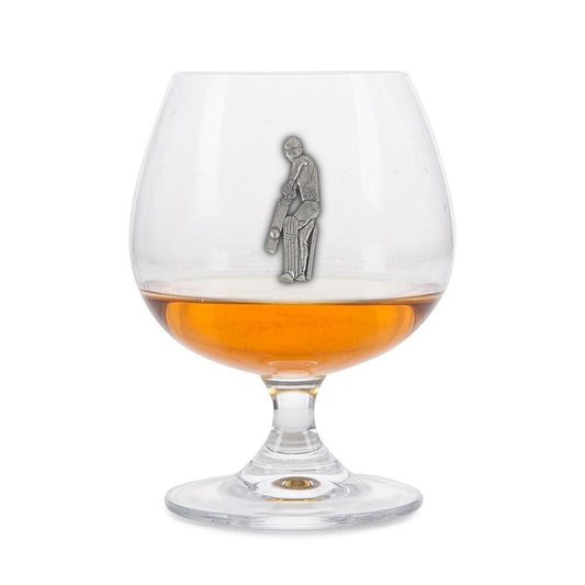 Crystal brandy glass with pewter cricket player emblem, partially filled with amber liquid