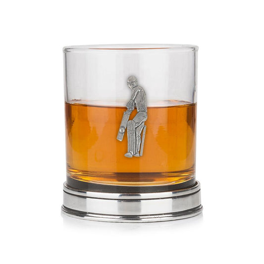 Whisky tumbler with pewter cricket player emblem and polished base, partially filled with amber liquid