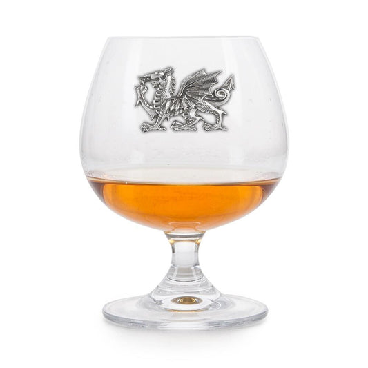 Crystal brandy glass with pewter Welsh Dragon emblem, partially filled with amber liquid