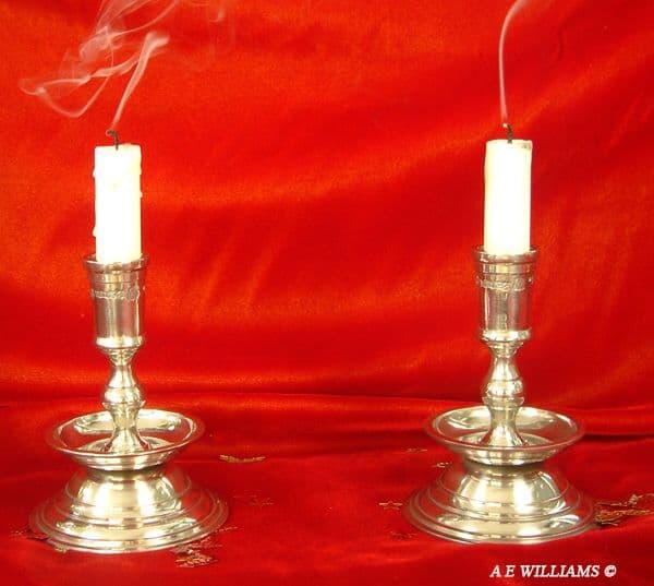 Silver candle holders with white candles and smoke, set against a red background.