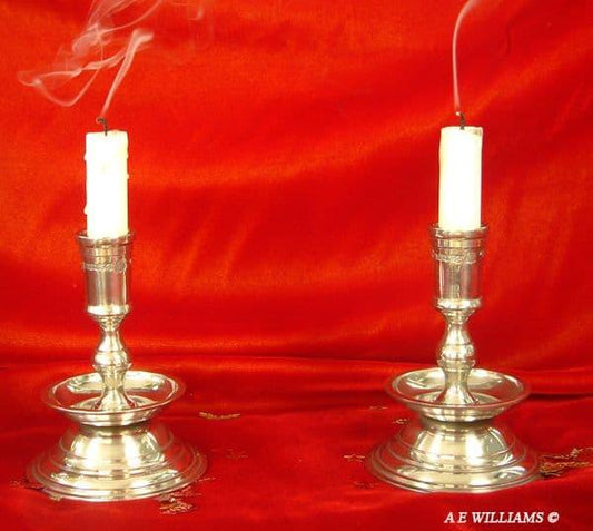 Silver candle holders with white candles and smoke, set against a red background.