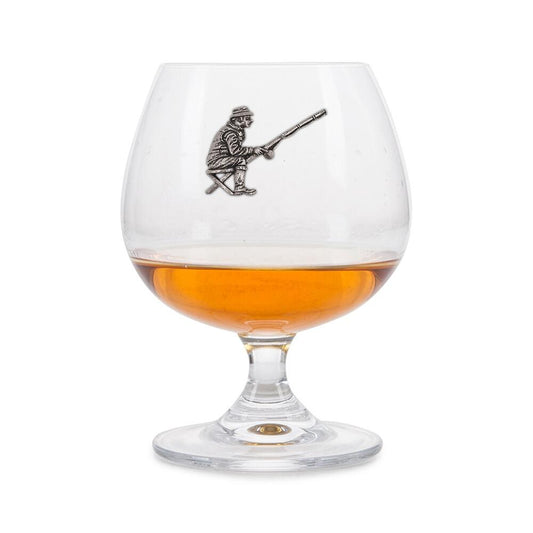 Crystal brandy glass with A E Williams pewter fisherman emblem, partially filled with amber liquid