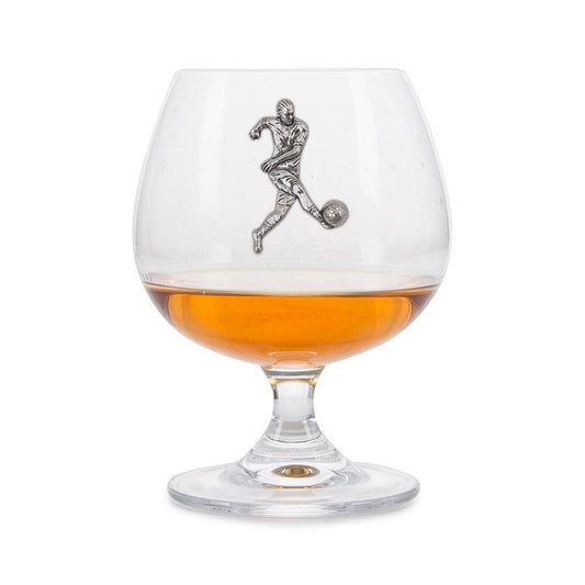 Crystal brandy glass with A E Williams pewter footballer emblem, partially filled with amber liquid