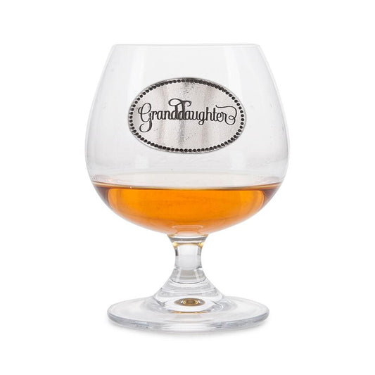Crystal brandy glass with A E Williams pewter "Granddaughter" emblem, partially filled with amber liquid