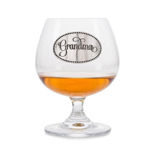 Crystal brandy glass with A E Williams pewter "Grandma" emblem, partially filled with amber liquid