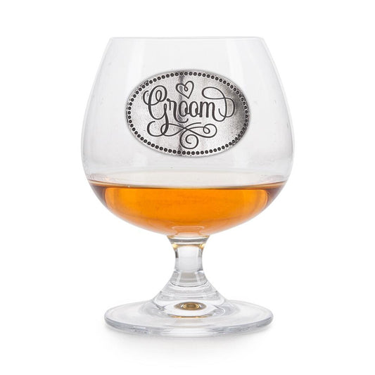 Crystal brandy glass with pewter "Groom" emblem, partially filled with amber liquid