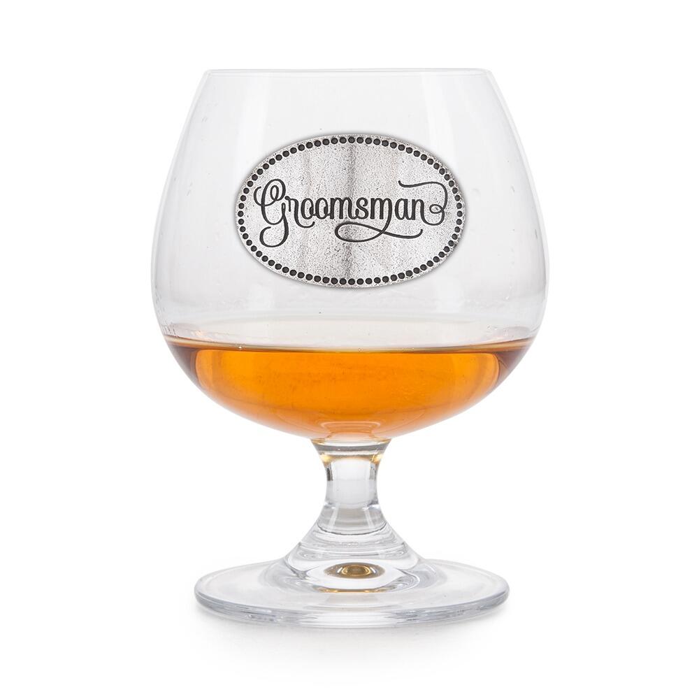 Elegant crystal brandy glass with pewter "Groomsman" badge, partially filled with amber liquid