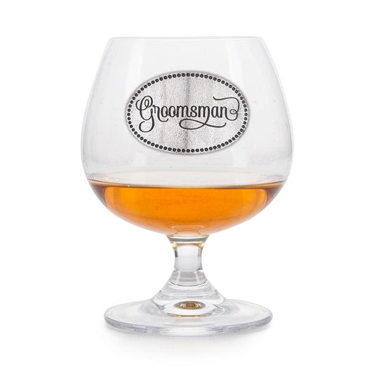 Elegant crystal brandy glass with pewter "Groomsman" badge, partially filled with amber liquid