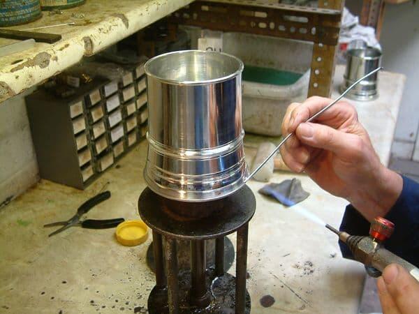 Shiny silver metal cup being crafted with a torch and tool in a workshop