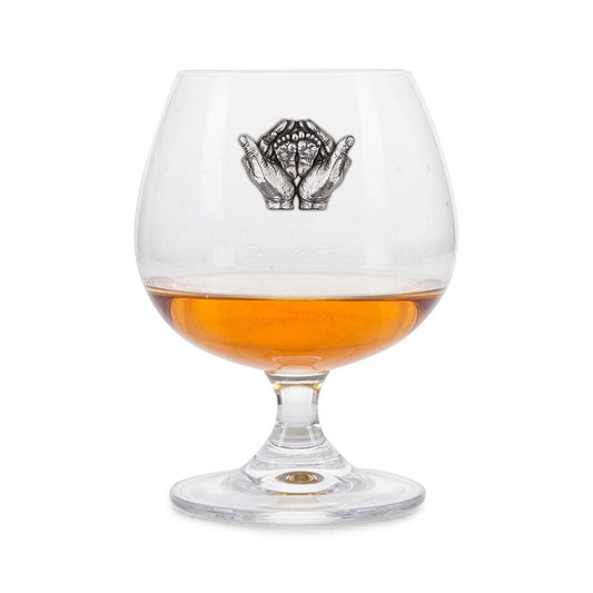 Crystal brandy glass with pewter emblem of hands holding baby feet, partially filled with amber liquid