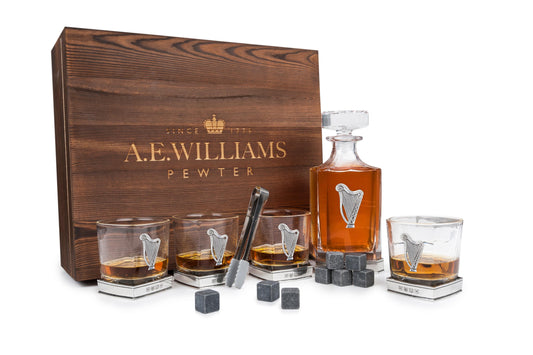 Wooden presentation box displaying decanter and four tumblers with pewter Irish Harp motifs, accompanied by whisky stones and tongs