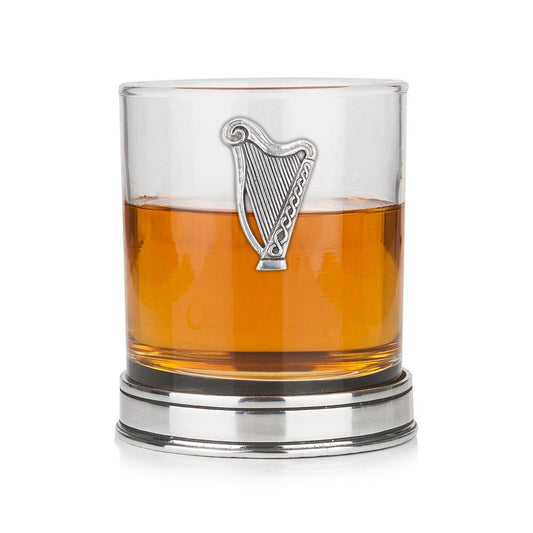 Whisky tumbler with pewter Irish Harp emblem and polished base, partially filled with amber liquid