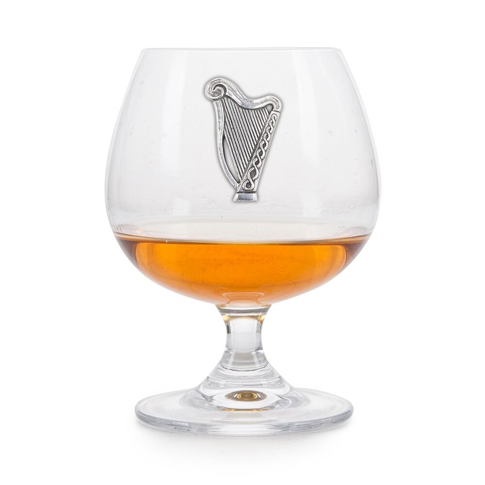 Crystal brandy glass with pewter Irish Harp emblem, partially filled with amber liquid