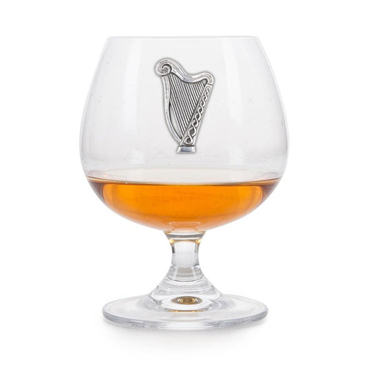 Crystal brandy glass with pewter Irish Harp emblem, partially filled with amber liquid