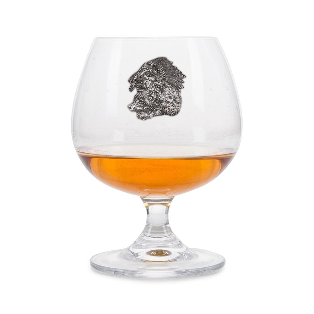 Crystal brandy glass with pewter Native American and wolf emblem, partially filled with amber liquid