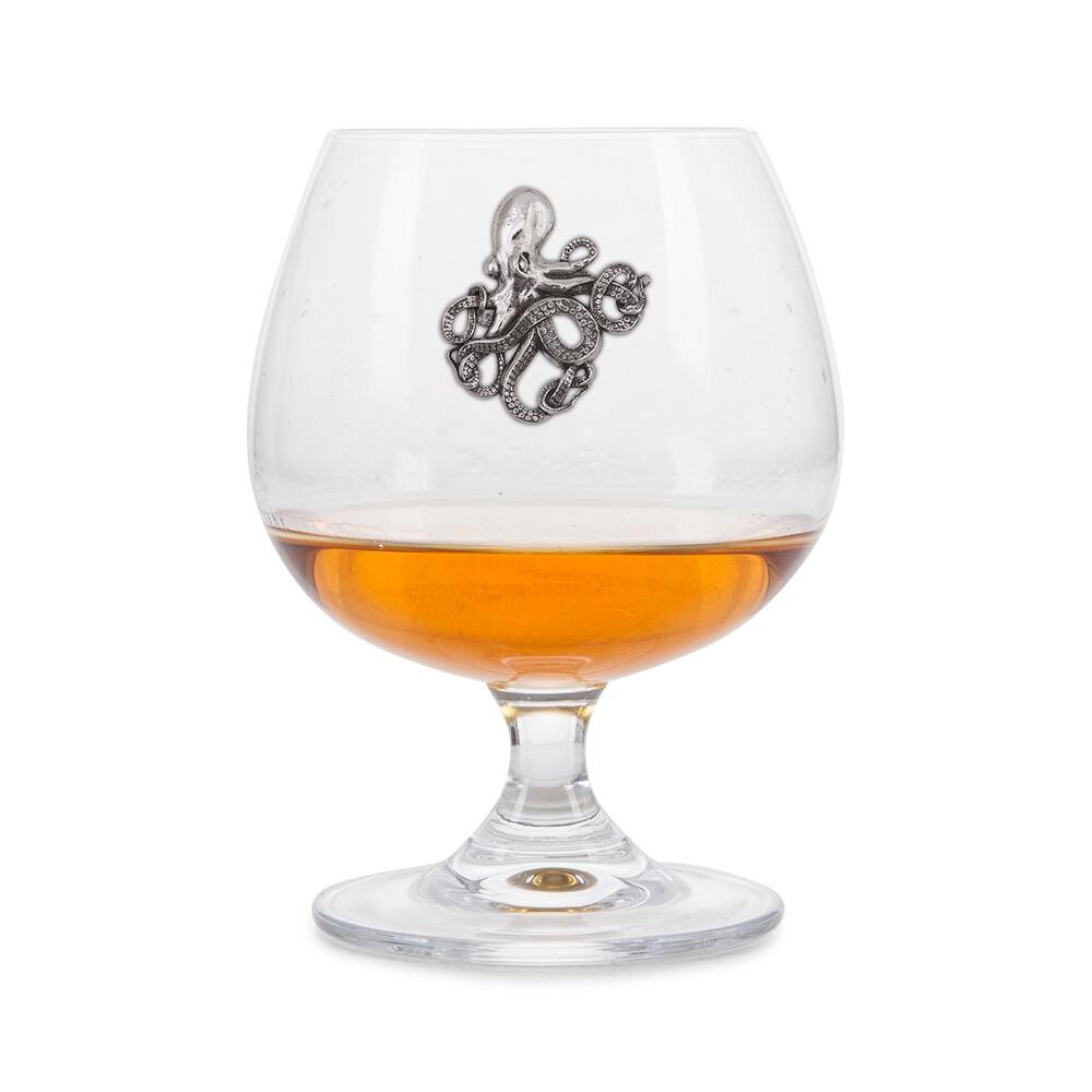 Crystal brandy glass with pewter octopus emblem, partially filled with amber liquid