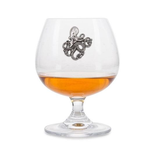 Crystal brandy glass with pewter octopus emblem, partially filled with amber liquid