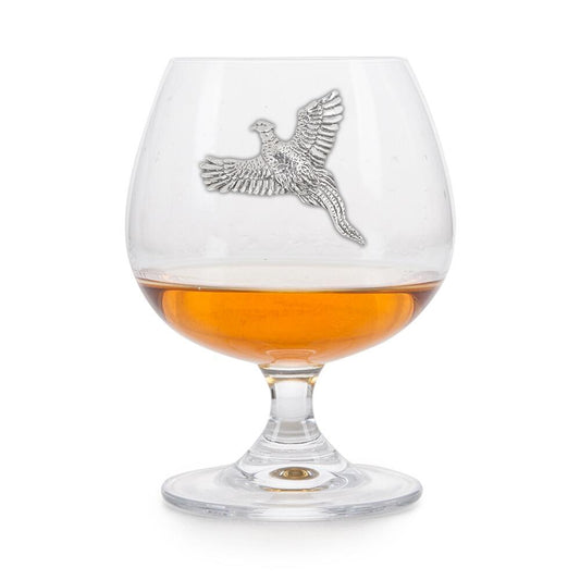 Crystal brandy glass with pewter pheasant emblem, partially filled with amber liquid
