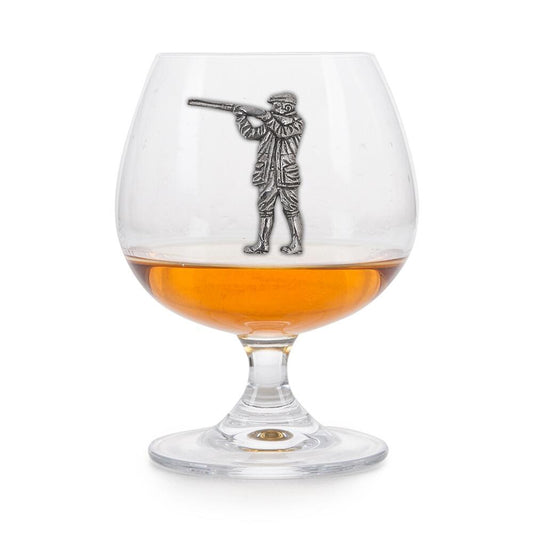 Crystal brandy glass with pewter shooting figure emblem, partially filled with amber liquid