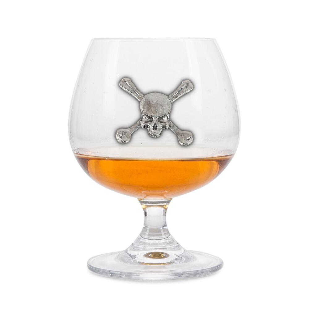 Crystal brandy glass with pewter skull and crossbones emblem, partially filled with amber liquid