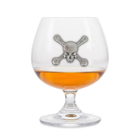 Crystal brandy glass with pewter skull and crossbones emblem, partially filled with amber liquid