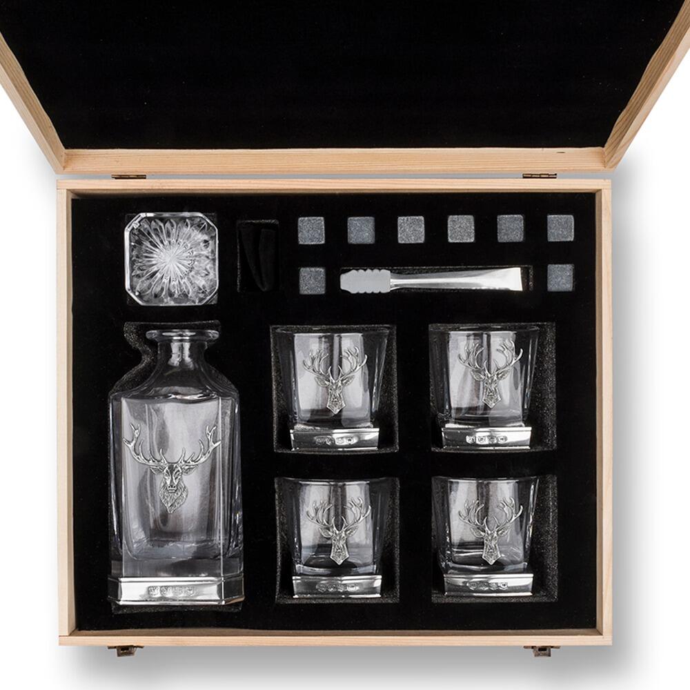 Overhead view of an opened wooden gift box containing a whiskey decanter with Stag, four glasses with Stag motifs, whiskey stones, and metal tongs, all arranged neatly in black foam padding"