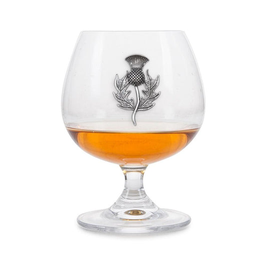 Crystal brandy glass with pewter Scottish Thistle emblem, partially filled with amber liquid