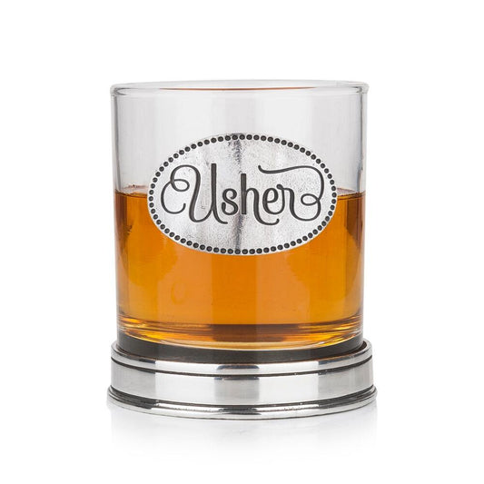 Whisky tumbler with pewter 'Usher' badge and polished base, partially filled with amber liquid