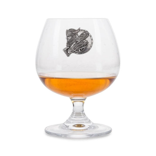 Crystal brandy glass with pewter Viking Warrior emblem, partially filled with amber liquid